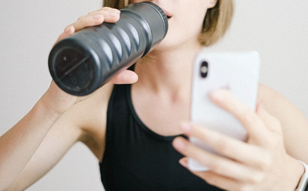 Female athlete drinking water and checking her phone